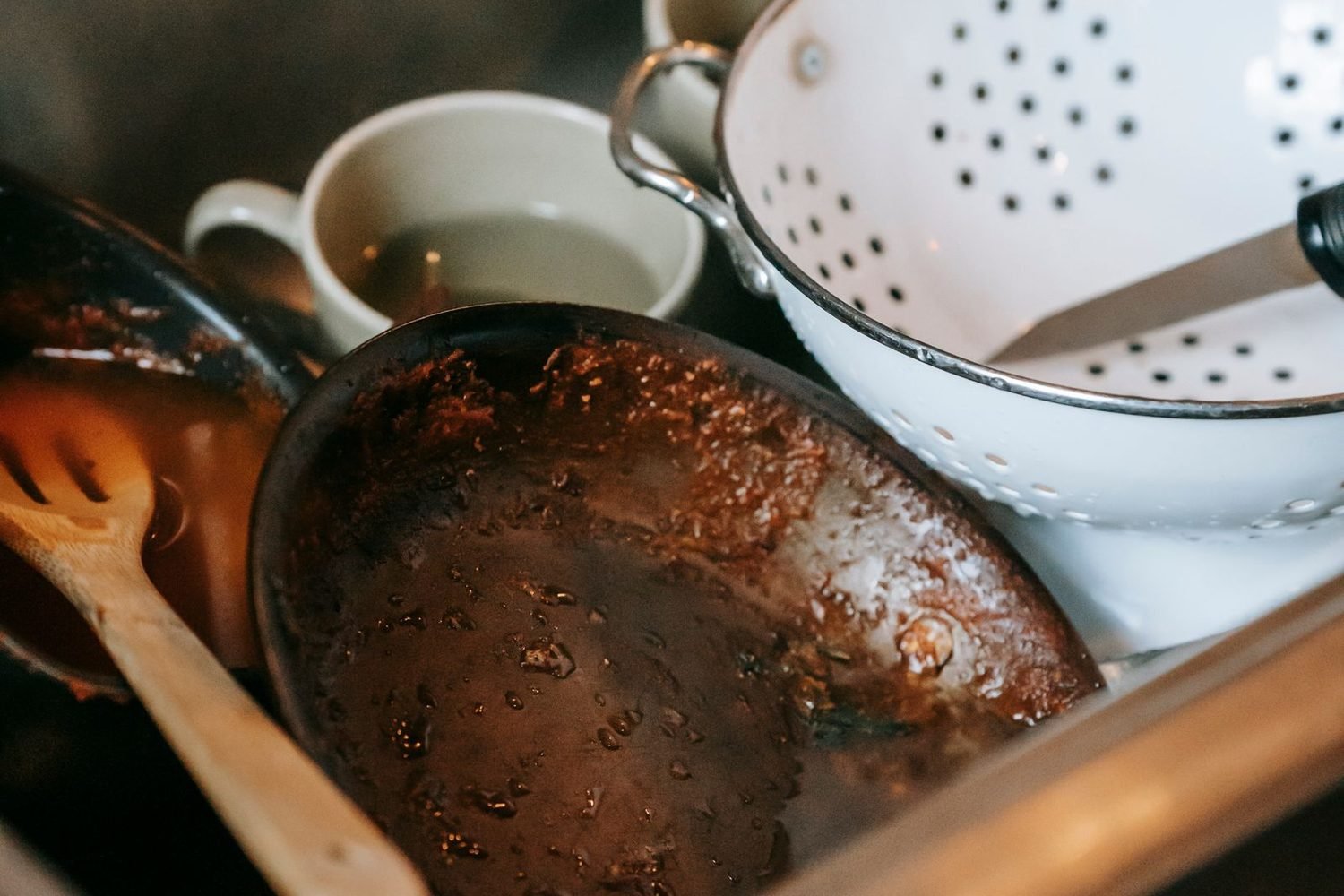 Breakroom sink piled with greasy, unwashed dishes before cleaning